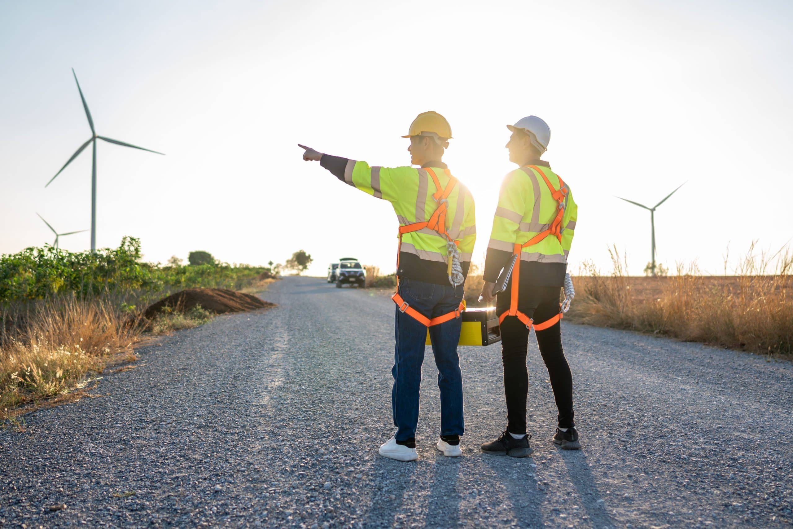 two men wearing safety vests and helmets standing on a road